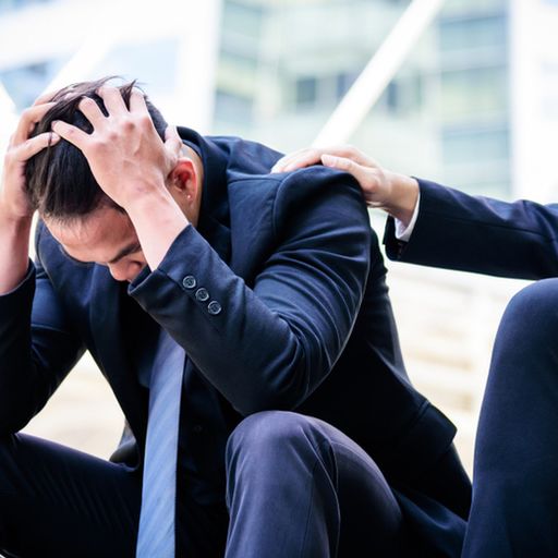 a man in a suit is comforting another man who is sitting on the ground .