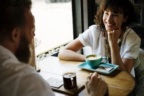 a man and a woman are sitting at a table with a cup of coffee .