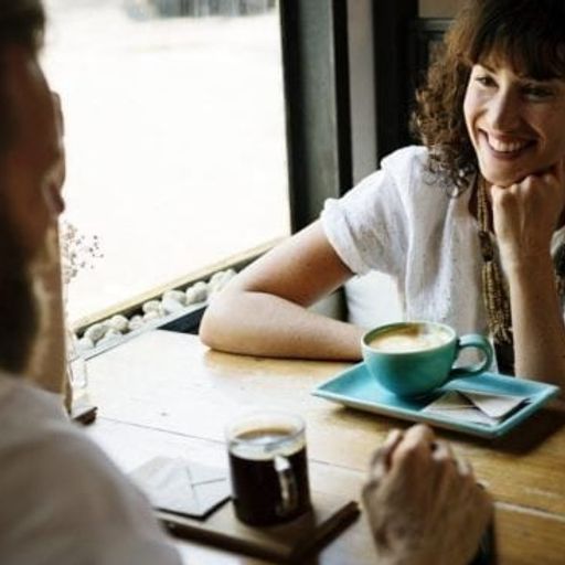 a man and a woman are sitting at a table with a cup of coffee .