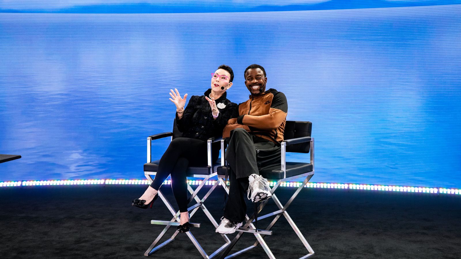 a man and a woman are sitting in director 's chairs in front of a body of water .