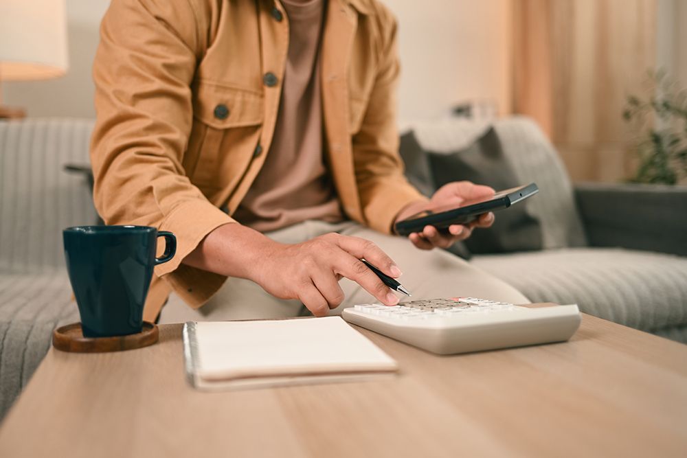 a man is sitting on a couch using a calculator and a cell phone .