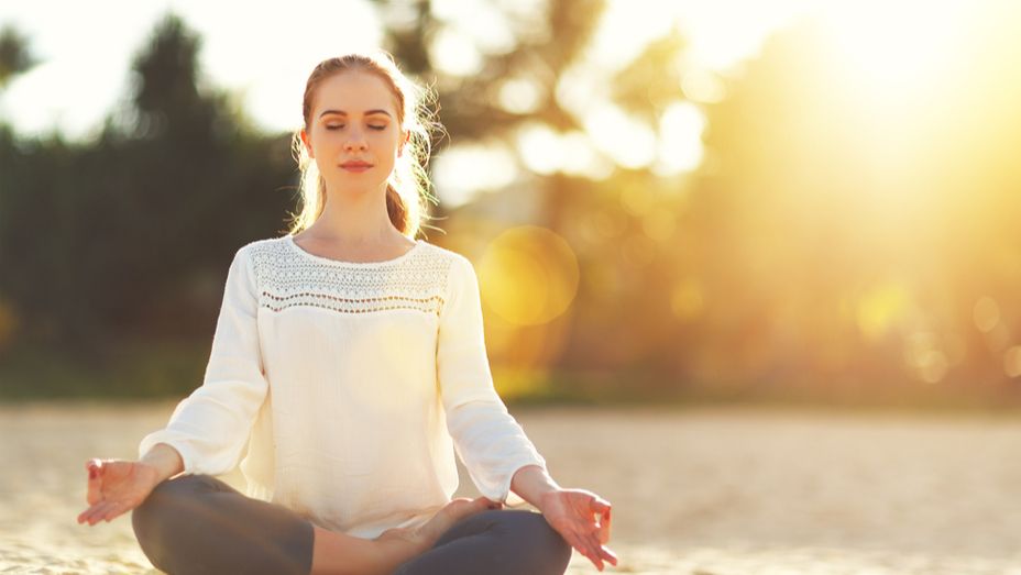 a woman is sitting in a lotus position on the beach with her eyes closed .
