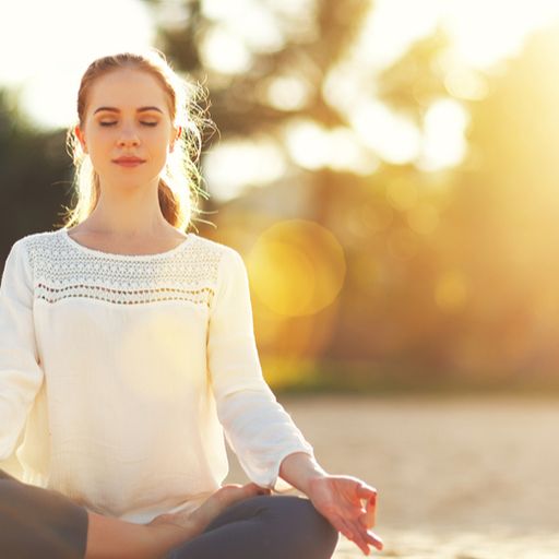 a woman is sitting in a lotus position on the beach with her eyes closed .