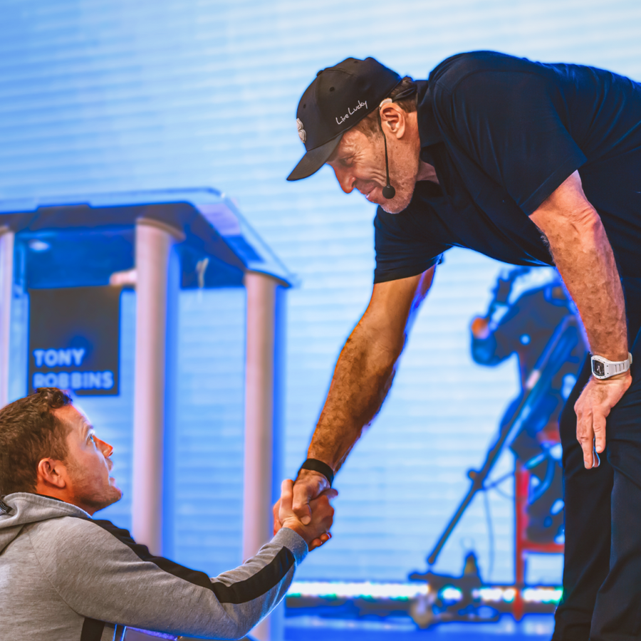 two men shake hands in front of a sign that says tony robbins