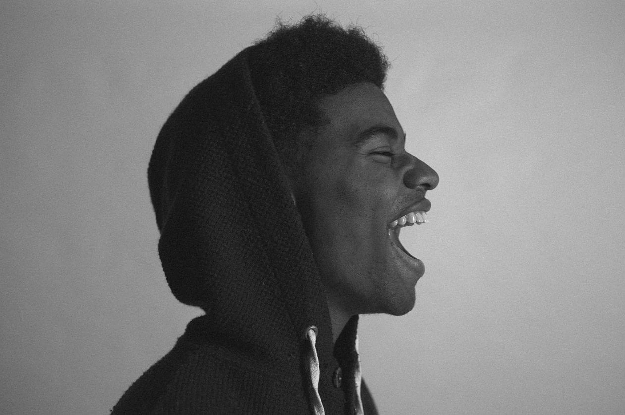 a black and white photo of a young man wearing a hoodie laughing .