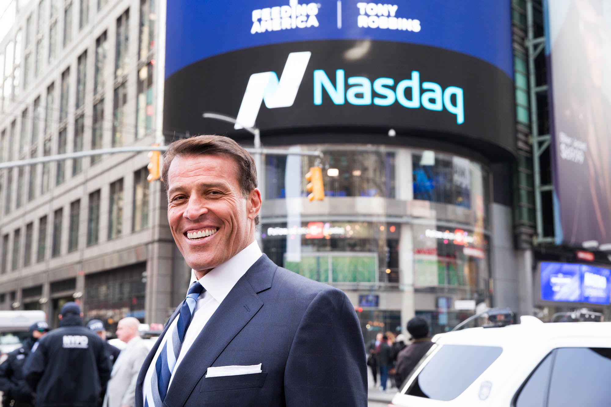 a man in a suit and tie is standing in front of a nasdaq building .
