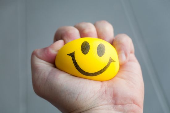 a person is holding a yellow stress ball with a smiley face on it .