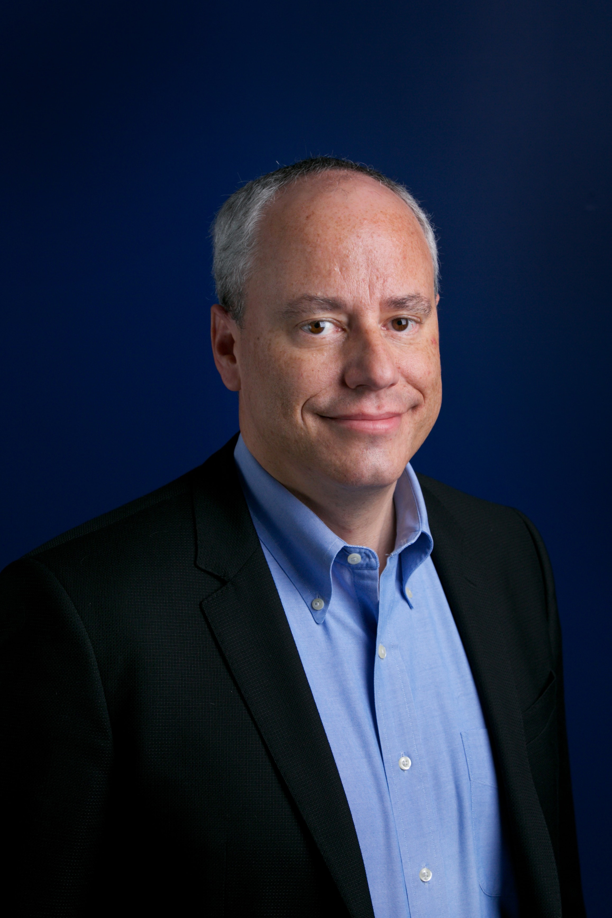 a man in a suit and blue shirt smiles for the camera