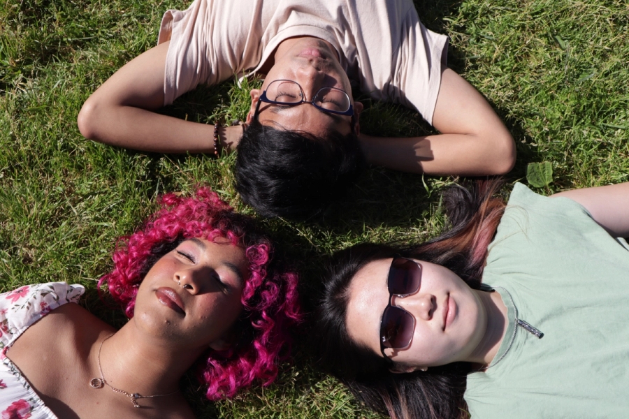 Two girls and a boy laying on grass.