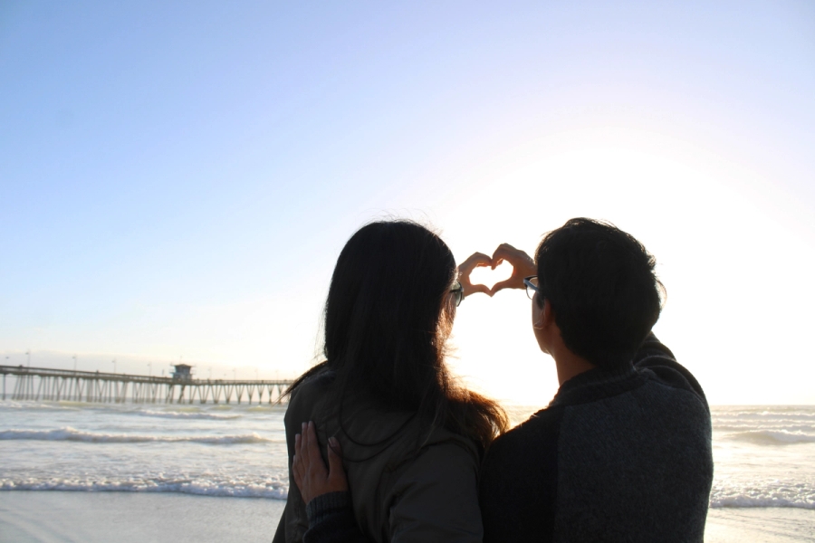 Back POV of girl and boy making a heart with their hands. 