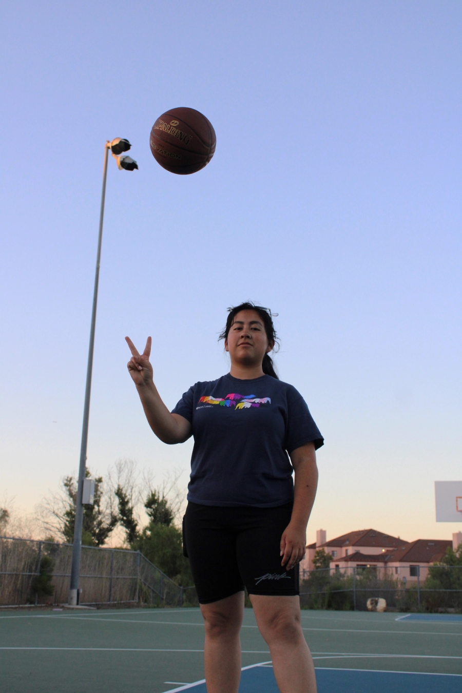 Girl holding up peace sign with ball in air.
