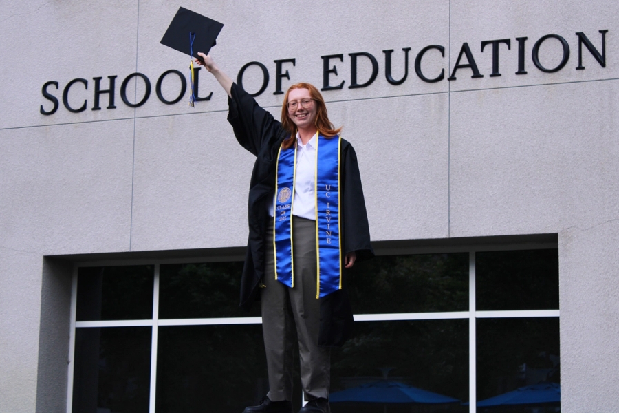 Girl standing near school sign with grad cap.