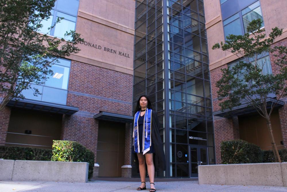 Girl in stoles and cords in front of brick building.