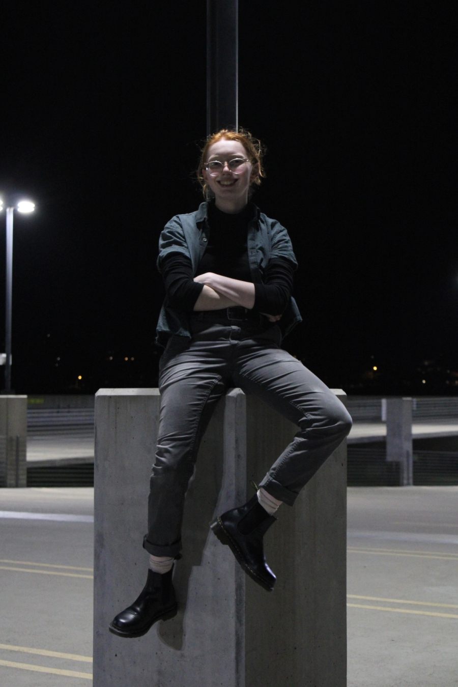 Girl sitting crossed arms on lamppost.