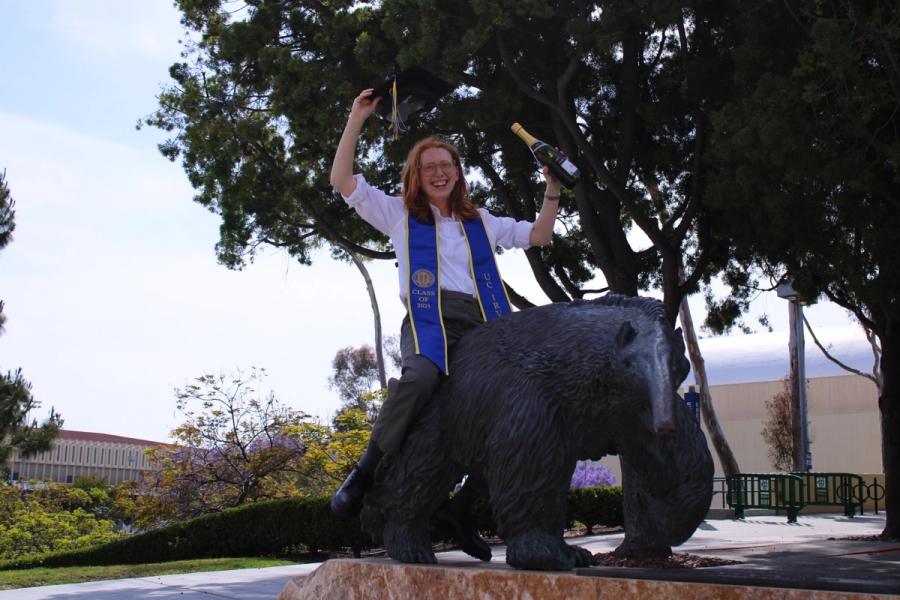 Girl sitting on anteater statue with cap and bottle.