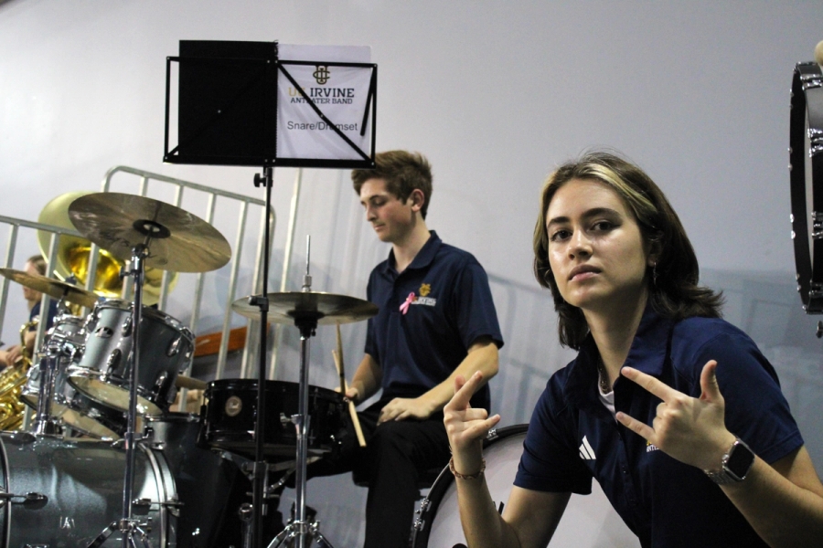 Girl with rock and roll signs and boy staring at drums.
