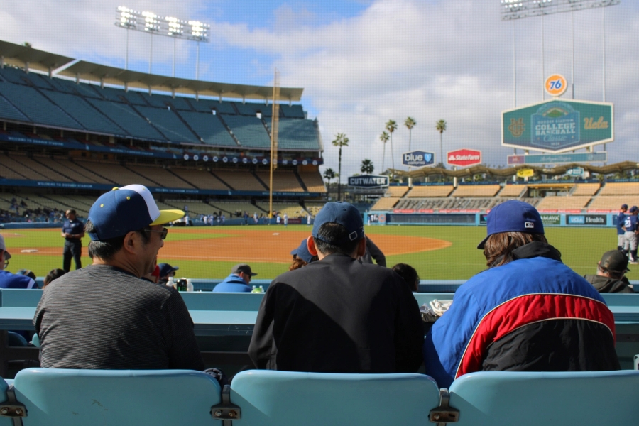 Back POV of UCLA baseball stadium behind three fans.