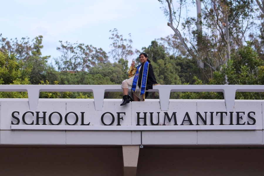 Girl sitting on School of Humanities sign.