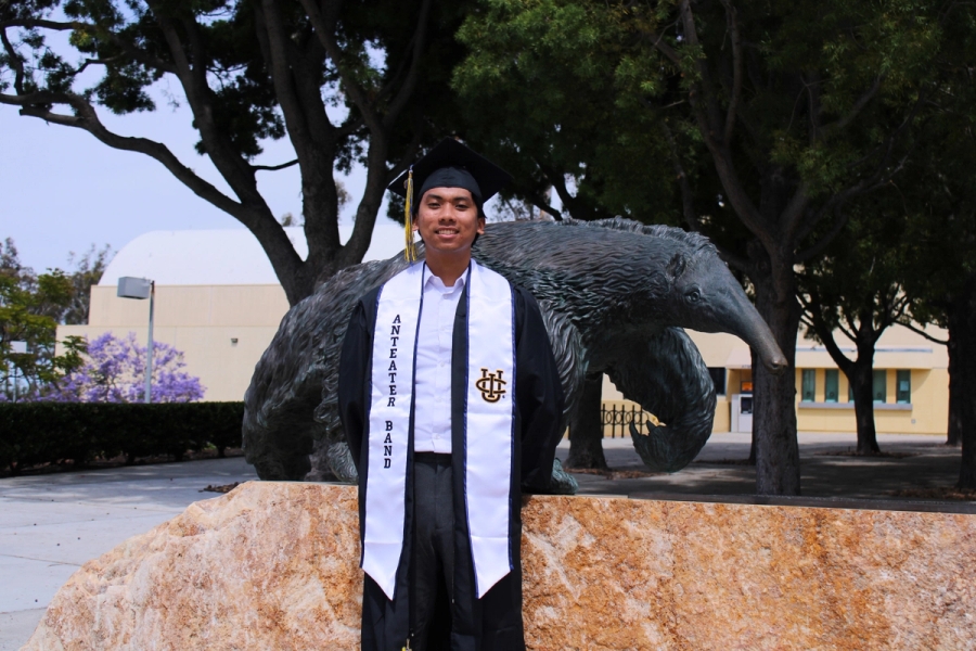Boy standing in grad fit in front of anteater statue.