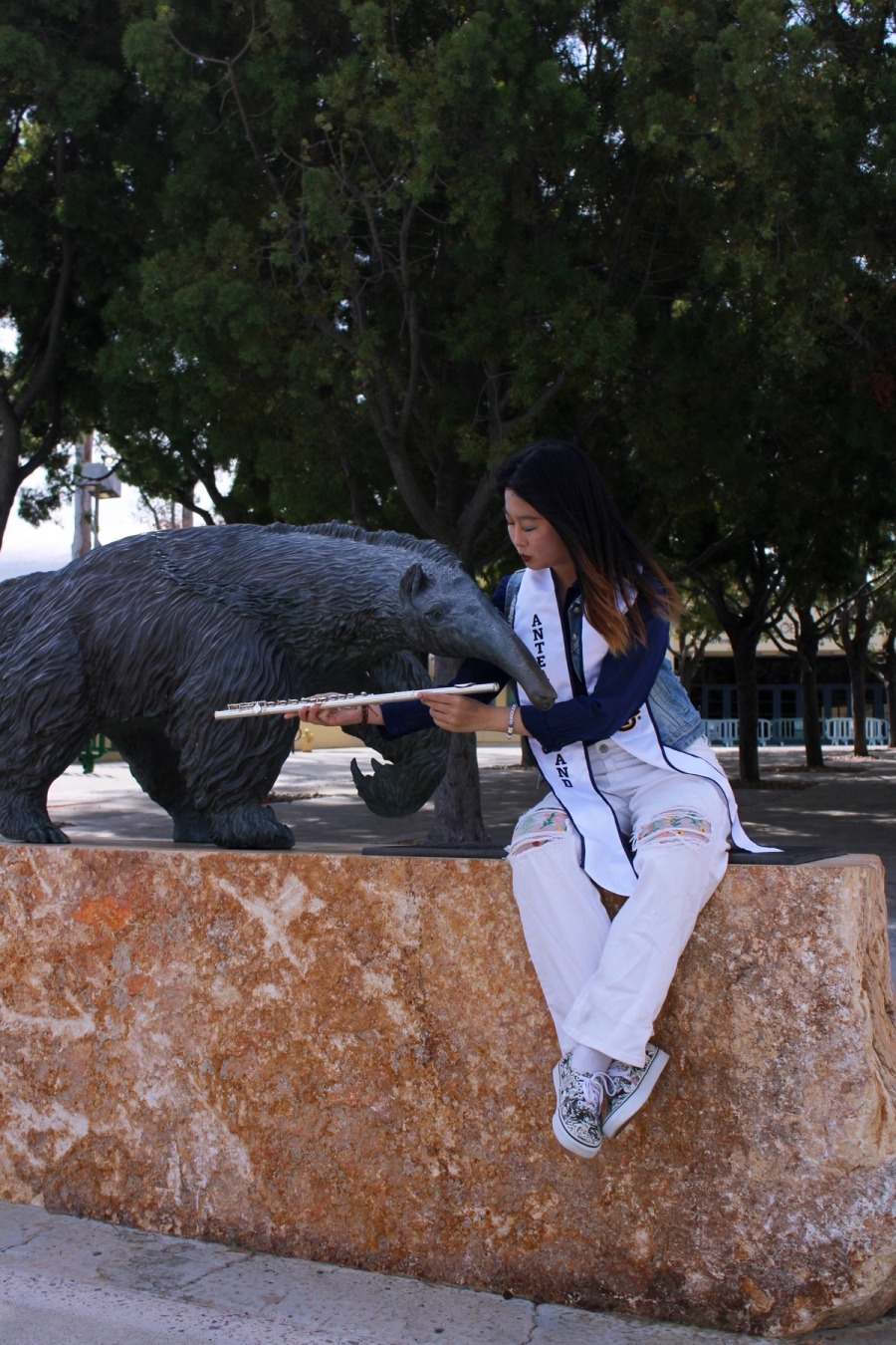 Girl teaching anteater statue how to play the flute.