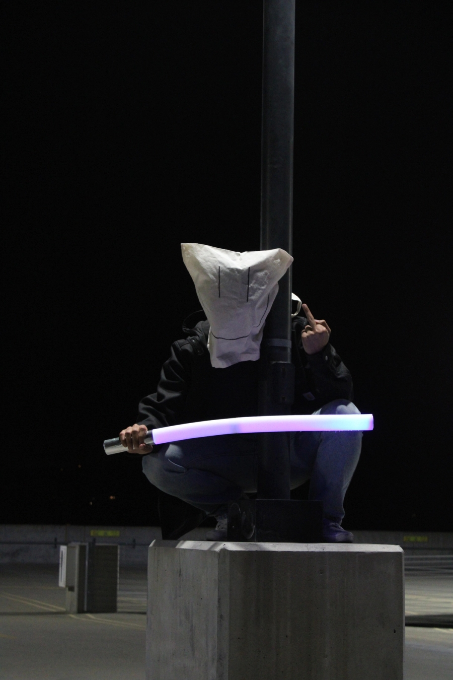 Guy with tote bag over head and light saber in hand on lamppost.