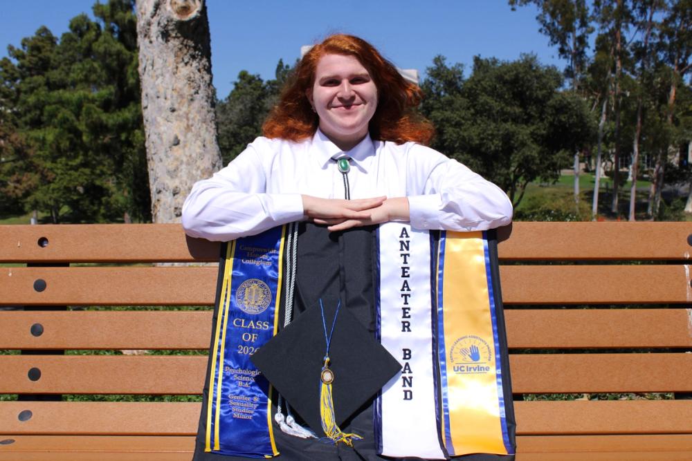 Guy posing with grad regalia on bench.