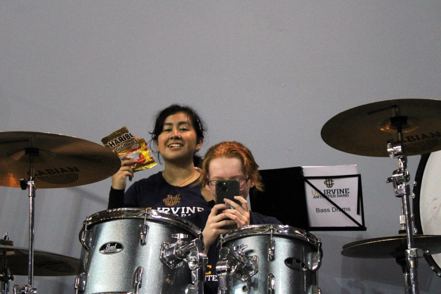 Girl on drums taking pic of camera and other girl eating gummy bears.