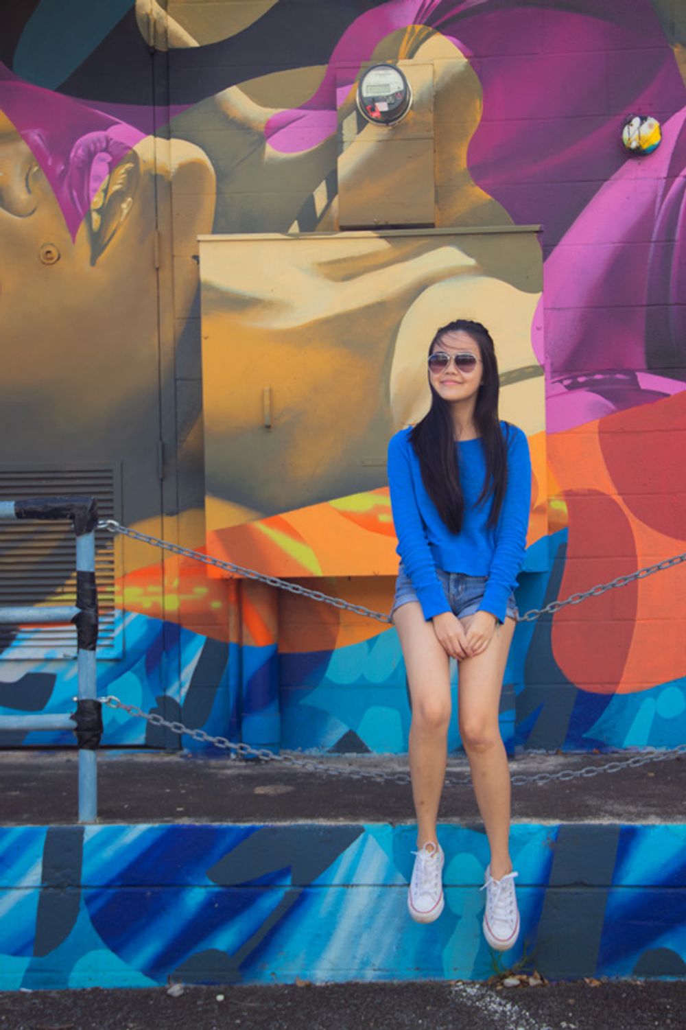 Girl sitting on a chain in front of a mural.