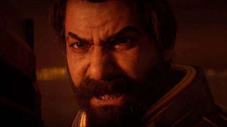 Saros: Close-up of a bearded man grimacing in a dim, orange-lit interior.