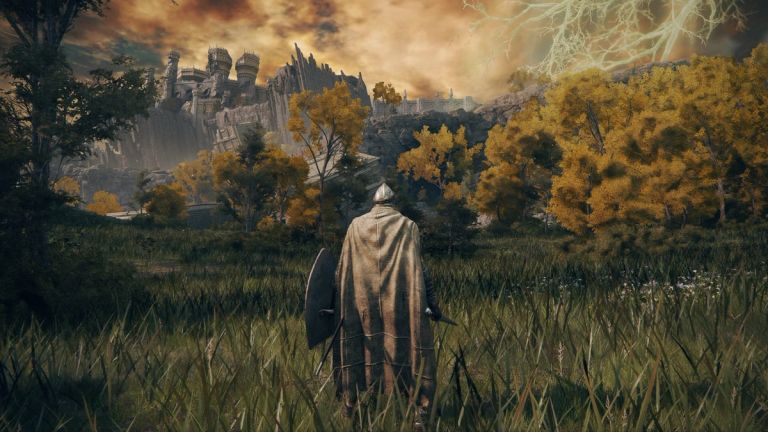 Elden Ring: A cloaked traveler with a shield stands in tall grass, facing a castle and golden-leaved trees.