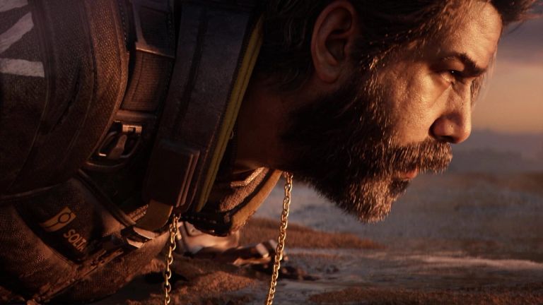 Saros: Close-up of a bearded man in dark armor leaning near the ground in warm light.