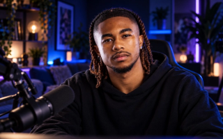 AI-generated image of DeenTheGreat with twisted hair in a black hoodie, sitting at a microphone in a neon-lit streaming studio