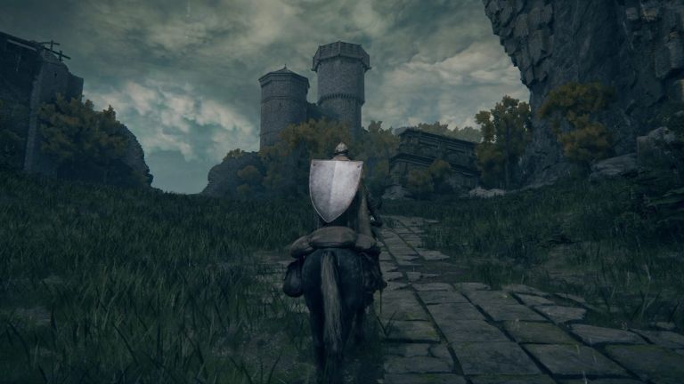 Elden Ring: An armored rider on a horse travels along a stone road toward ruined towers.