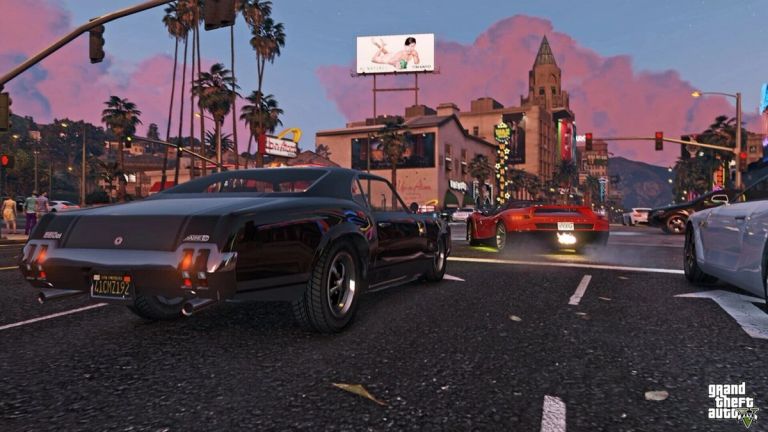 Several cars drive through a city street beneath a pink evening sky.