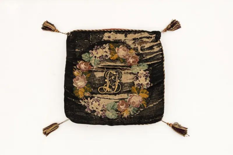 Díványpárna keresztöltéses, színes virágos díszítéssel, középen „L. J.” monogrammal, négy sarkán egy-egy bojttal, műbőr keretes