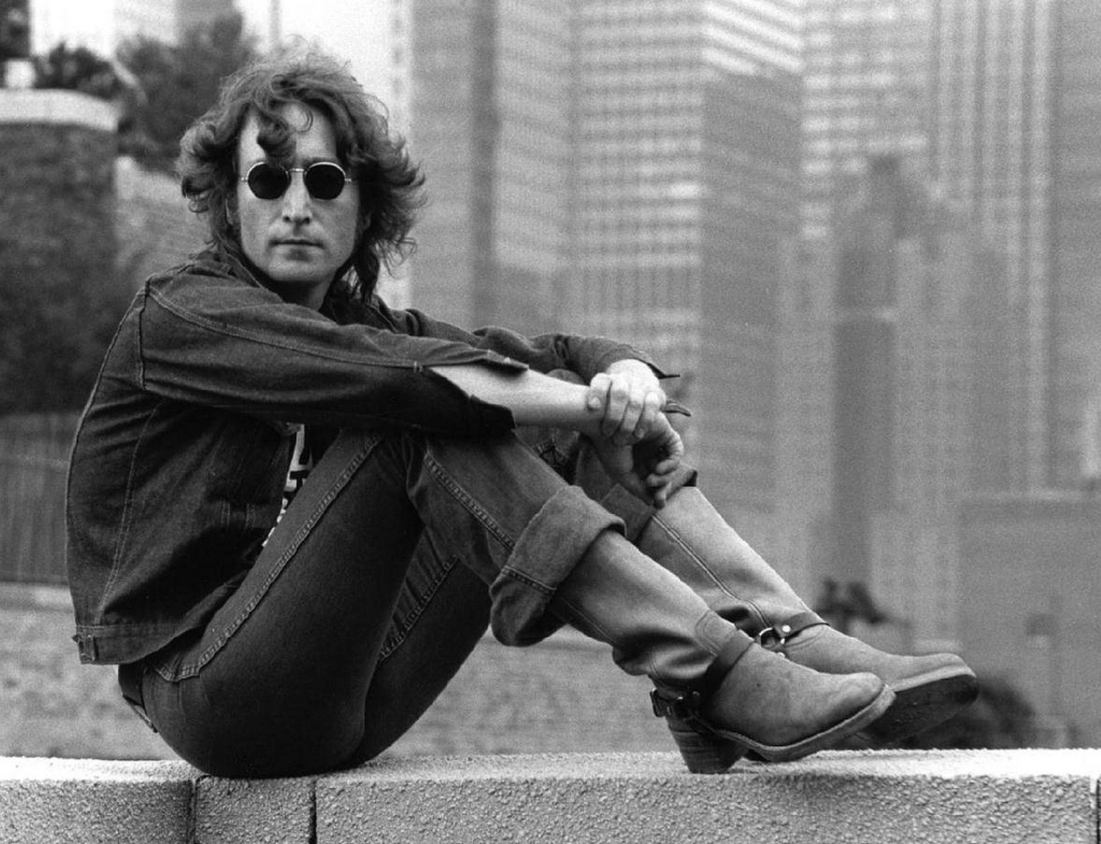 Der Musiker John Lennon sitzt auf einer Mauer