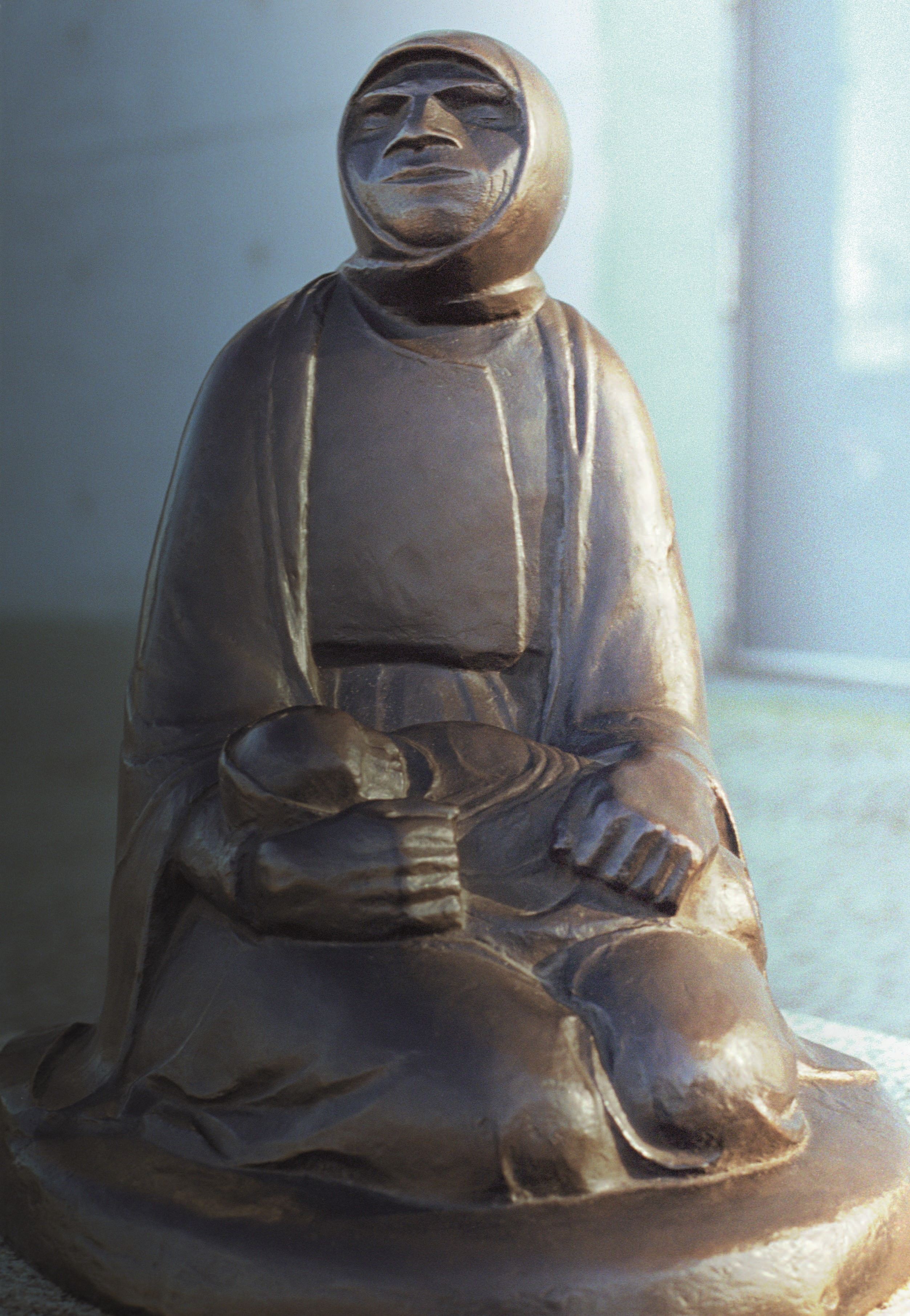 Frau mit Kopftuch am Boden sitzend ein Baby im Schoß