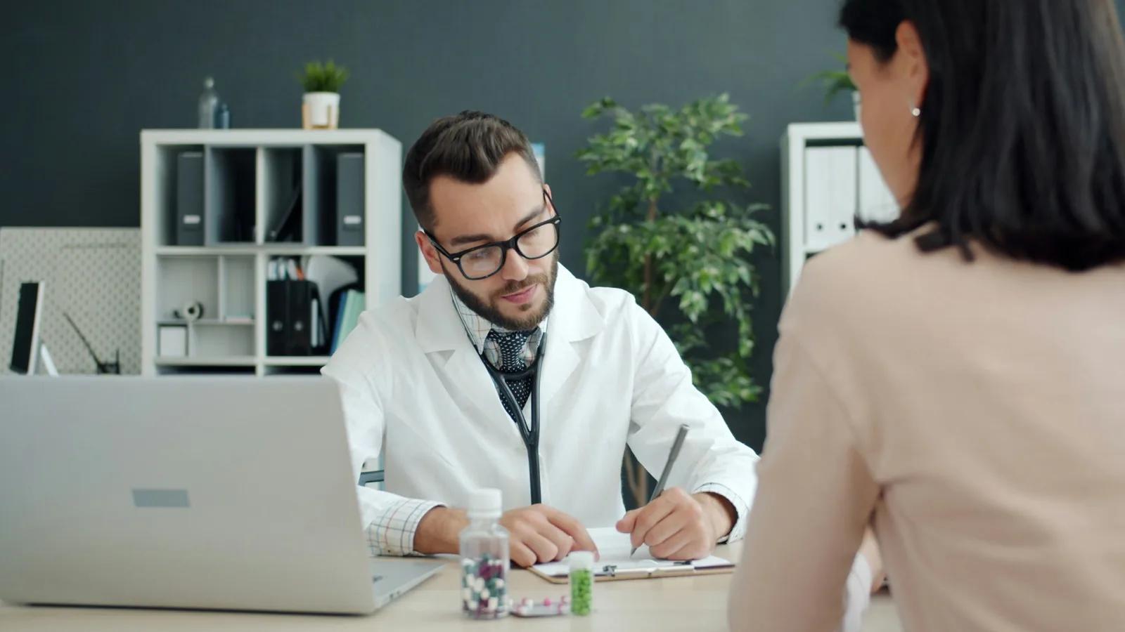 Doctor writing notes while patient sits opposite.
