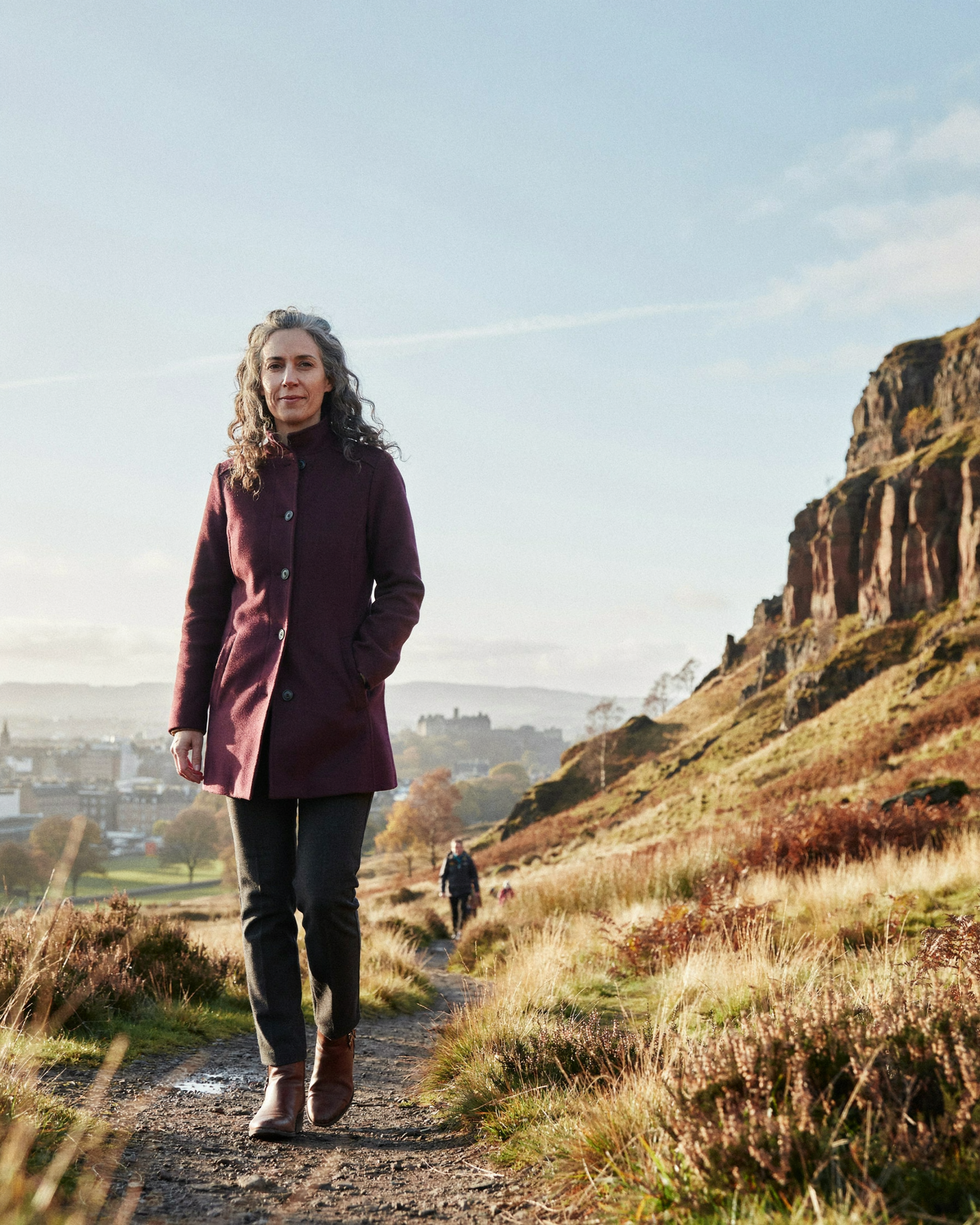 Adult walking beneath Salisbury Crags in Holyrood Park, Edinburgh, on an autumn morning, staying well through the COVID-19 vaccination season
