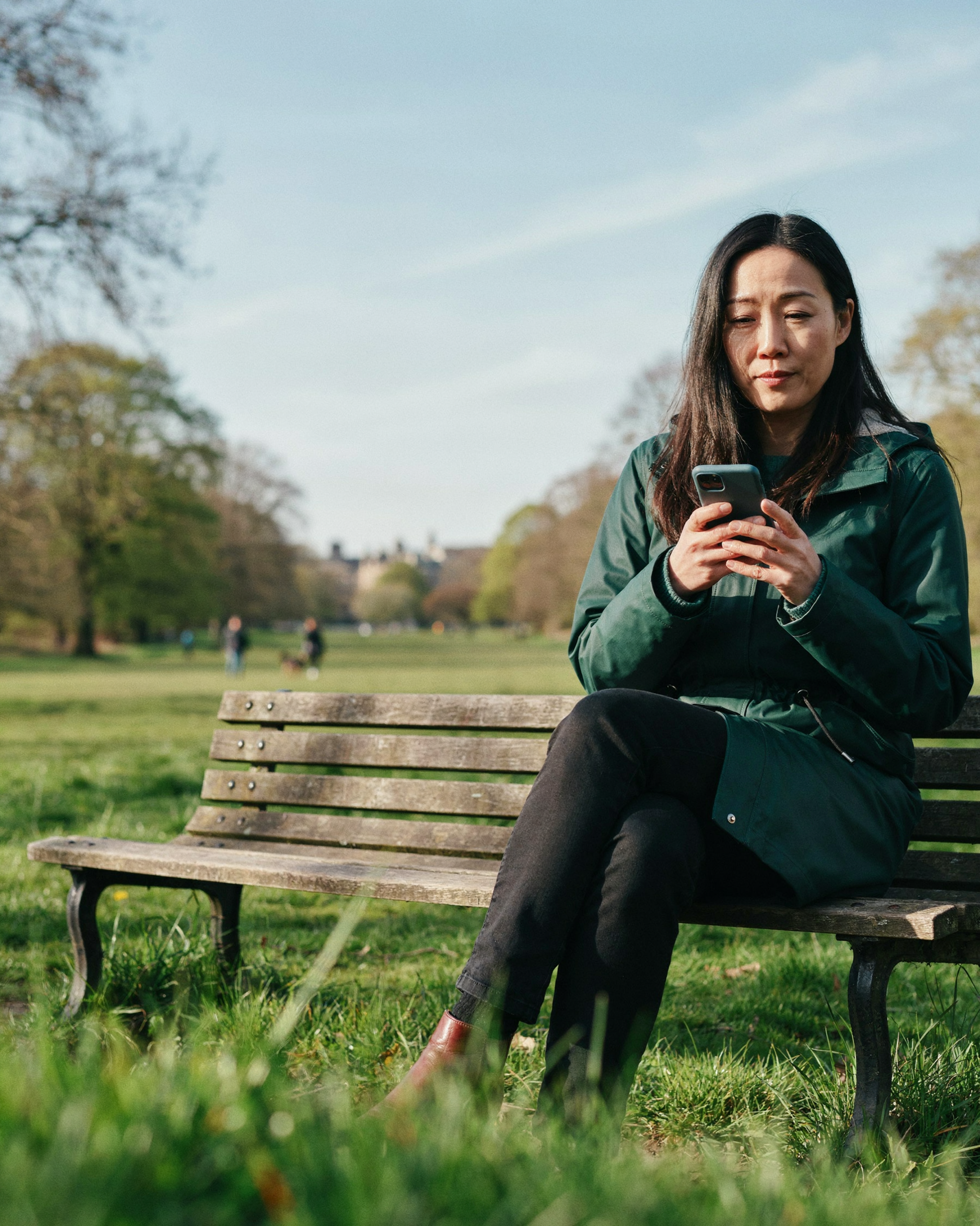 Adult sitting on a bench in the Meadows in Edinburgh, researching weight management options on their phone