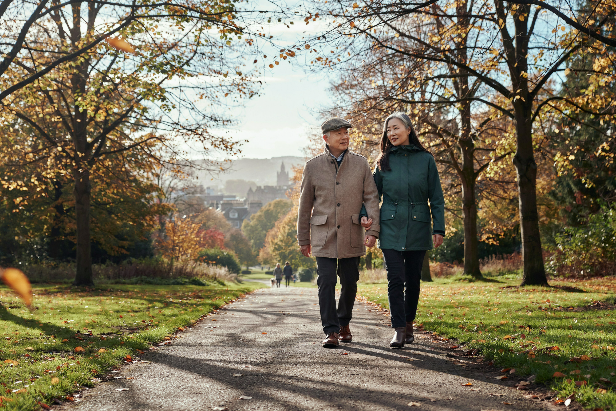 Adult walking arm in arm with their father, aged over 75, in Inverleith Park, Edinburgh, both protected for winter with a COVID-19 vaccine