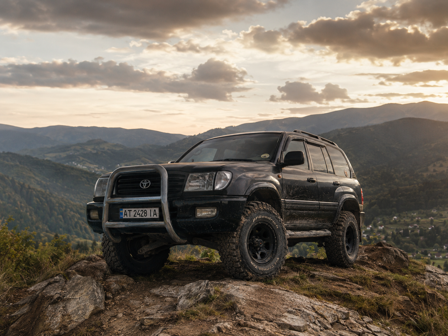Toyota Land Cruiser 100 темного кольору на скелястому виступі над лісистою долиною