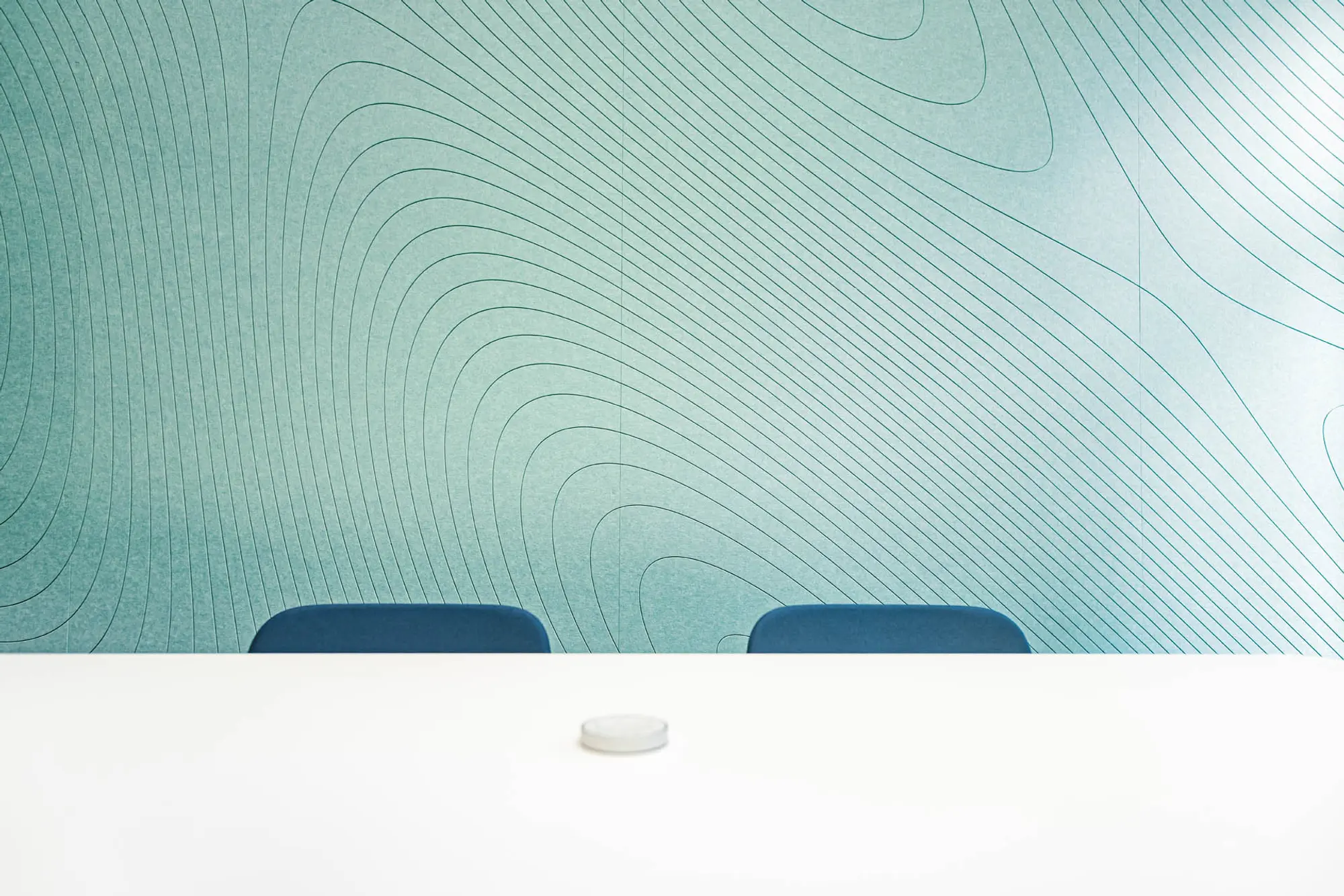 Heller Office Meetingraum mit hellgrüner Akustikverkleidung, weißem Meetingtisch und blauen Stühlen