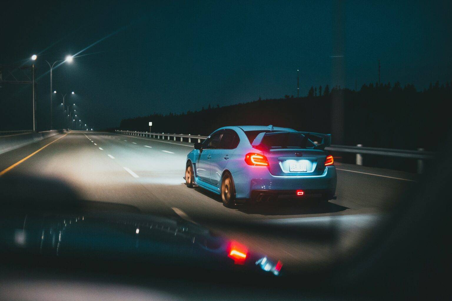 Blue car driving down road with headlights on