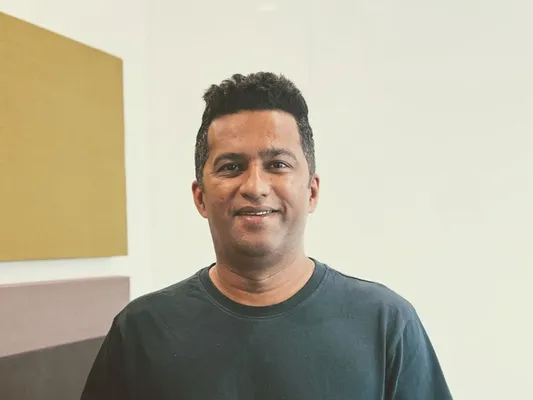 Smiling man in a dark t-shirt against a light wall with colored panels.