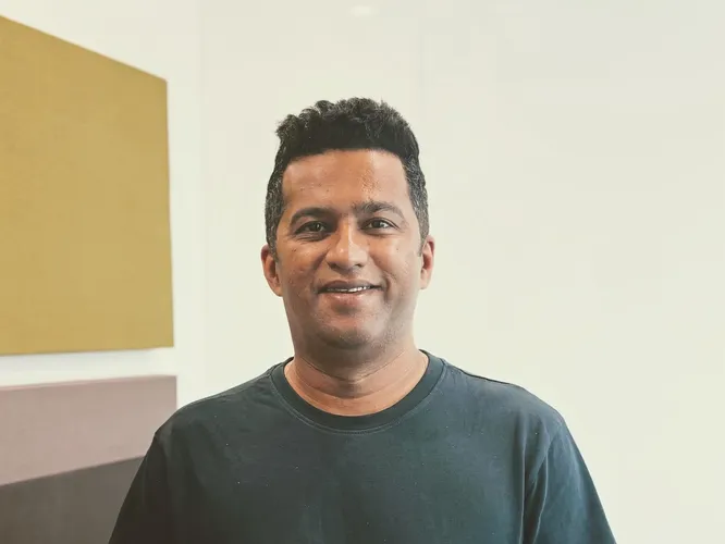 Smiling man in a dark t-shirt against a light wall with colored panels.