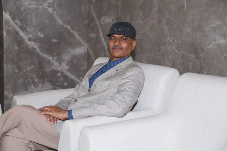 A man in a cap and blazer sits on a white sofa.
