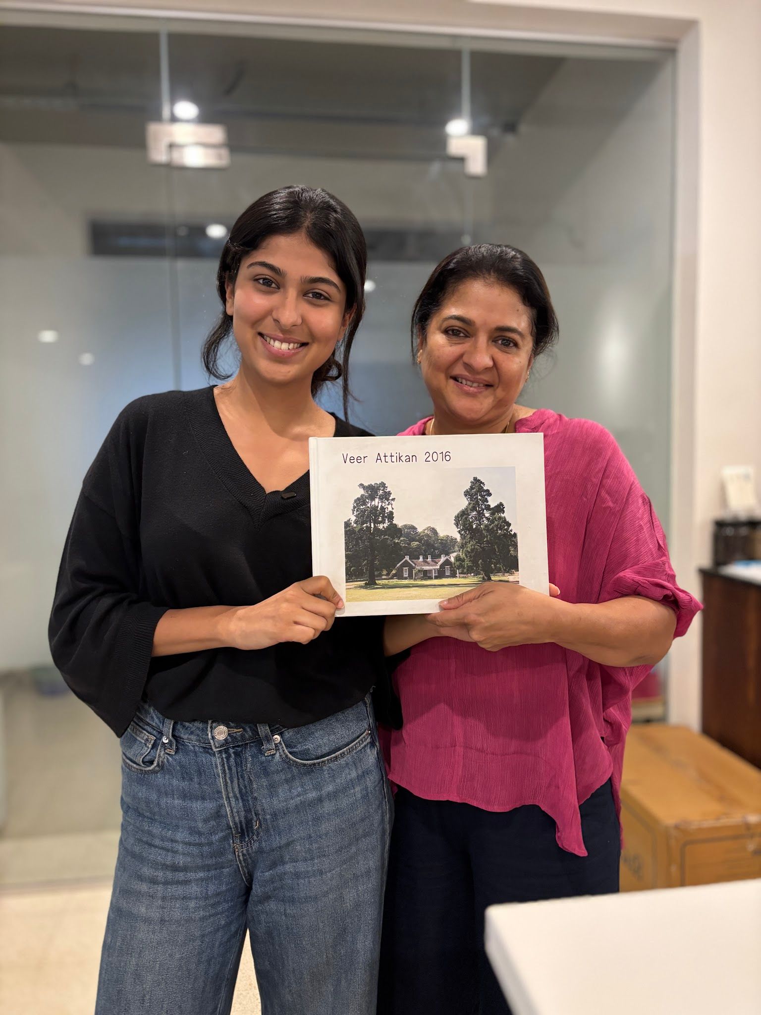 Two smiling women hold a book titled "Veer Attikan 2016" with a house on its cover.