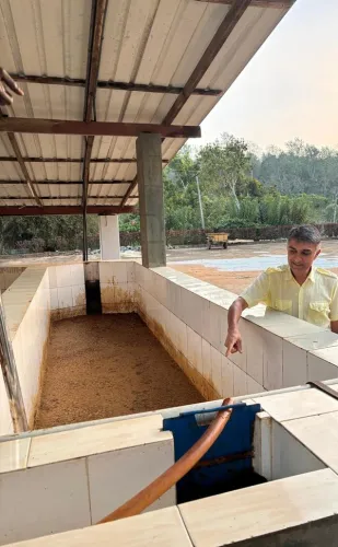 A man points into a large tiled vat filled with brown granular material at an agricultural processing facility.
