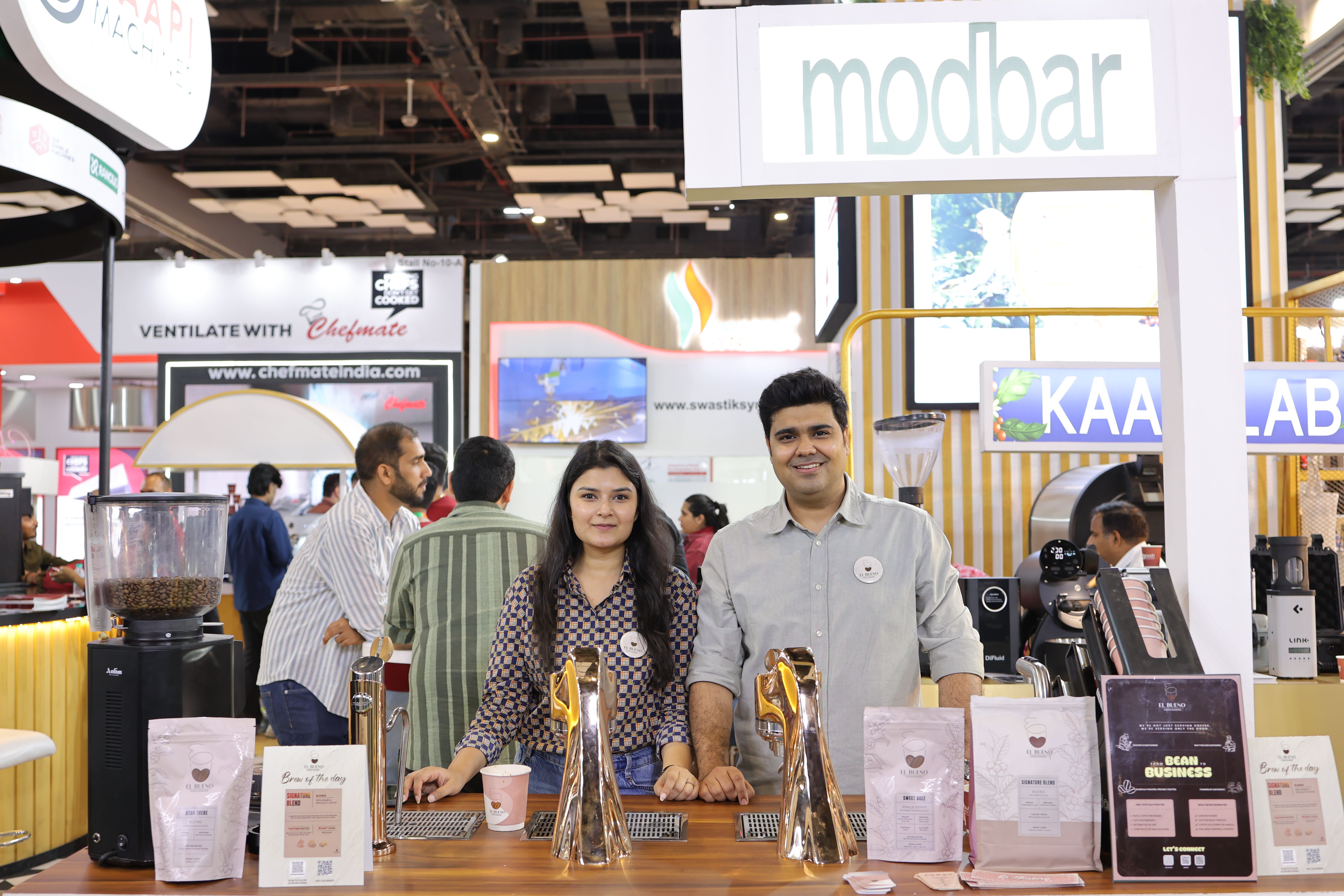 A smiling man and woman behind a Modbar coffee booth counter.